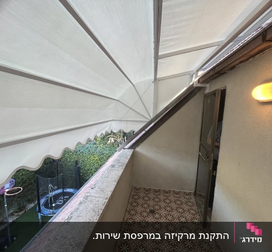 סוכך לבן נפתח מעל מרפסת עם קיר אבן
